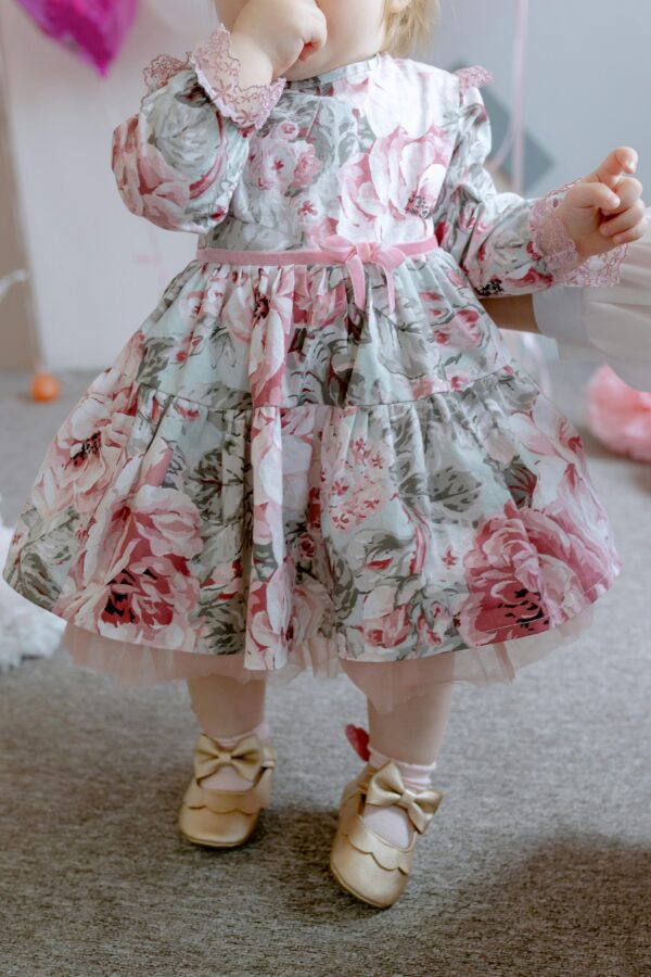 Charming toddler wearing a floral dress with bow shoes in an indoor setting.